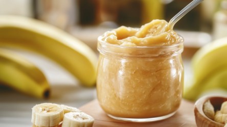 Ein Glas Bananengelee. Drumherum sind Bananen zu sehen.