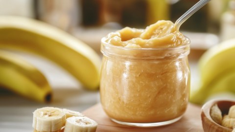 Ein Glas Bananengelee. Drumherum sind Bananen zu sehen.