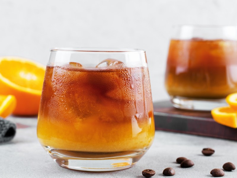 Zwei Gläser Bumble Coffee mit Eiswürfeln. Daneben liegen Orangen und Kaffeebohnen.