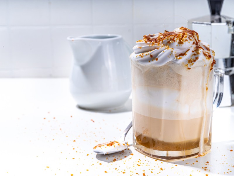 Glas mit Crème-brûlée-Latte, Espressokocher im Hintergrund