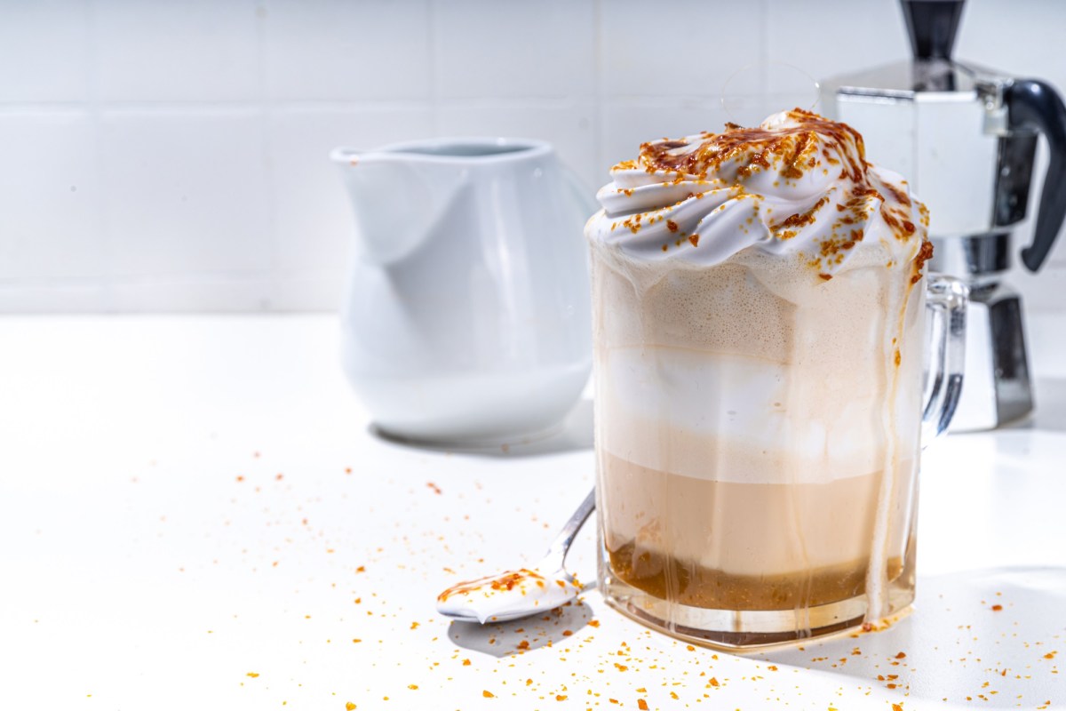 Glas mit Crème-brûlée-Latte, Espressokocher im Hintergrund