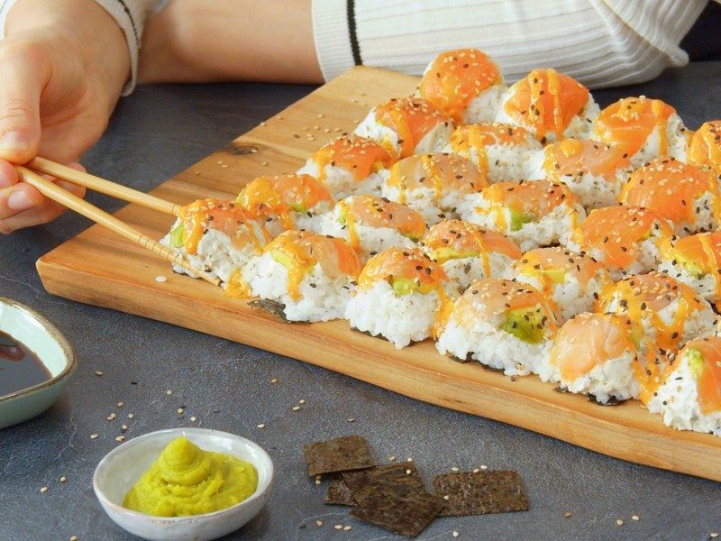 Jemand isst Eierkarton-Sushi von einem Holzbrett mit zwei Esstäbchen.