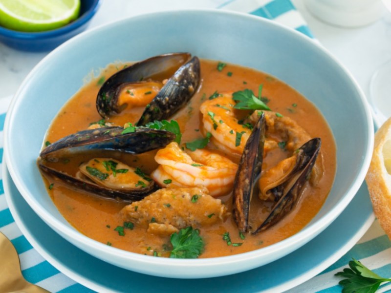 Eine Schüssel mit französischer Fischsuppe Bouillabaisse. Daneben 2 Scheiben Baguette.
