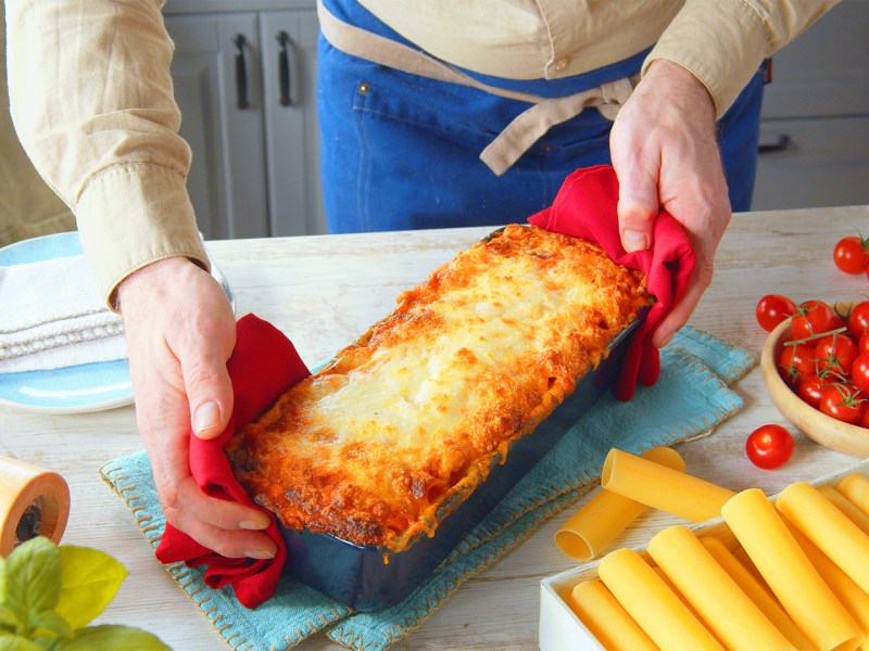 Ein Koch präsentiert eine Kastenform mit gefüllten Cannelloni mit Mozzarella.