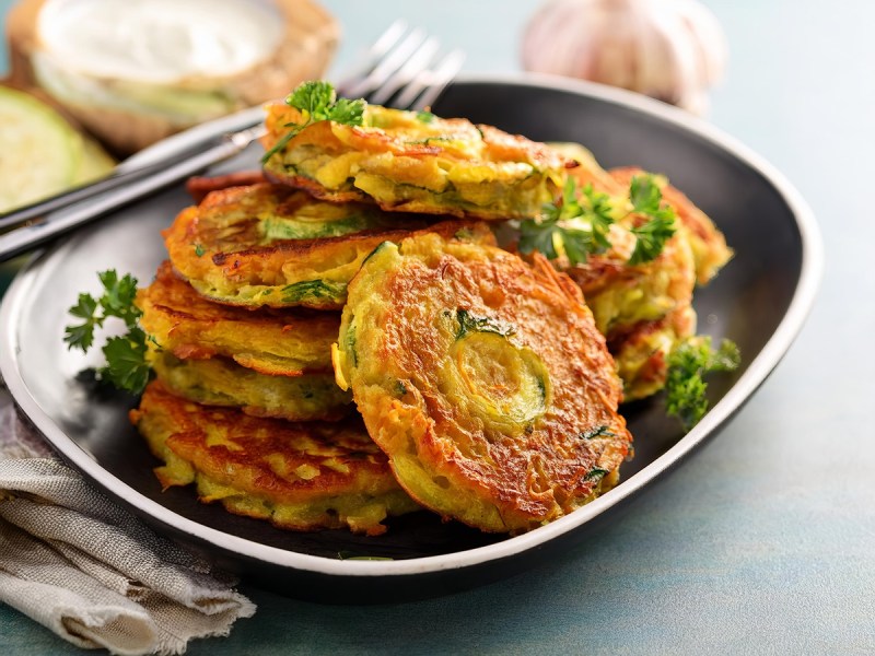 Gemüse-Rösti auf einem dunklen Teller, garniert mit krauser Petersilie.