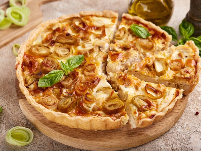 Hähnchen-Lauch-Quiche, von deer einige Stücke geschnitten wurden, auf einem Holzbrett.