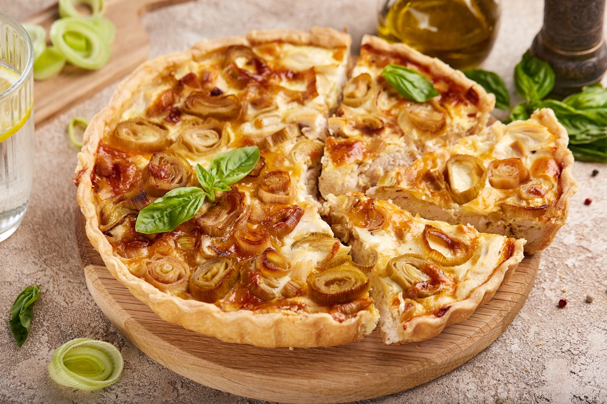 Hähnchen-Lauch-Quiche, von deer einige Stücke geschnitten wurden, auf einem Holzbrett.