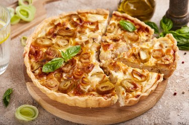 Hähnchen-Lauch-Quiche, von deer einige Stücke geschnitten wurden, auf einem Holzbrett.