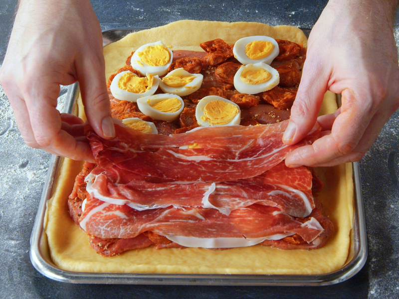 Ein Koch belegt den Boden einer spanischen Fleischpastete mit Schinken.
