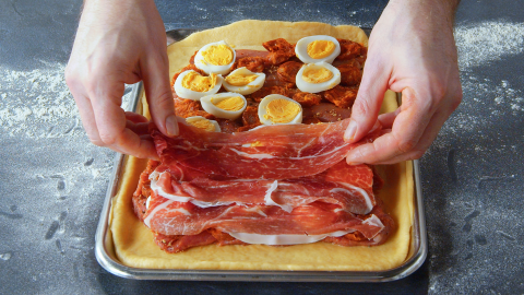 Ein Koch belegt den Boden einer spanischen Fleischpastete mit Schinken.