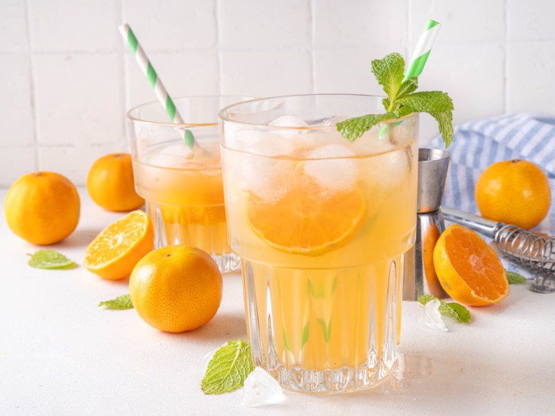 Glas mit Mandarinen-Minz-Limonade und Mandarinen daneben auf einem Tisch