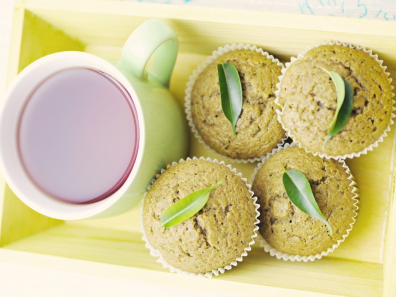 Mehrere Matcha-Muffins neben einer Tasse Tee in der Draufsicht.