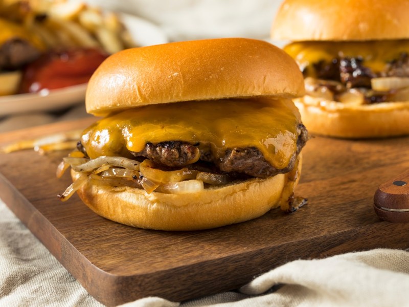 Mehrere Oklahoma Onion Burger auf einem Holzbrett.