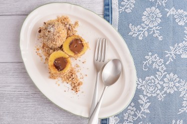 Schoko-Quark-Klöße, einer aufgeschnitten, mit Besteck auf einem ovalen Teller in der Draufsicht.