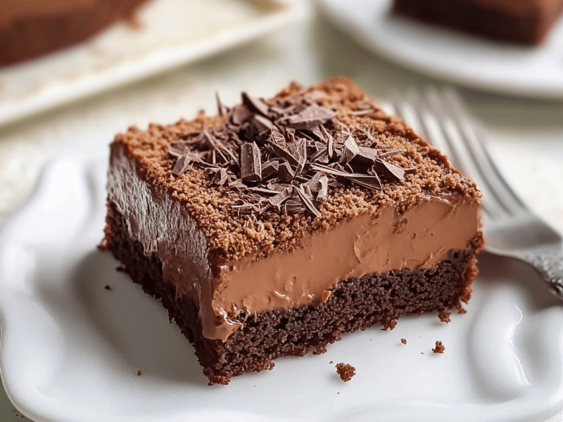 Ein Stück Schokopuddingschnitten vom Blech auf einem weißen Teller. Daneben liegt eine Gabel.