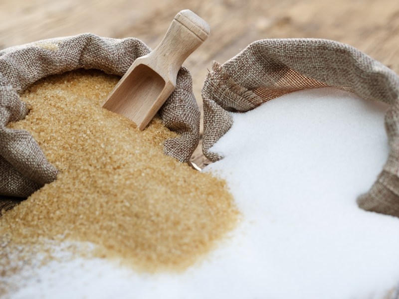 Unterschied brauner und weißer Zucker: Zwei Zuckersäcke mit braunem und weißem Zucker liegen nebeneinander. Der Zucker vermischt sich etwas.
