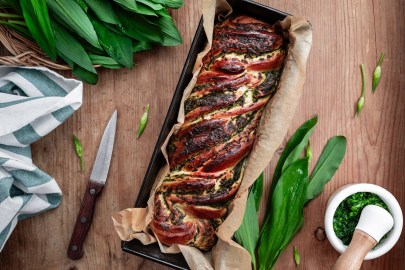 Bärlauch-Hefezopf in einer Kastenform. Daneben liegt Bärlauch sowie ein Messer.