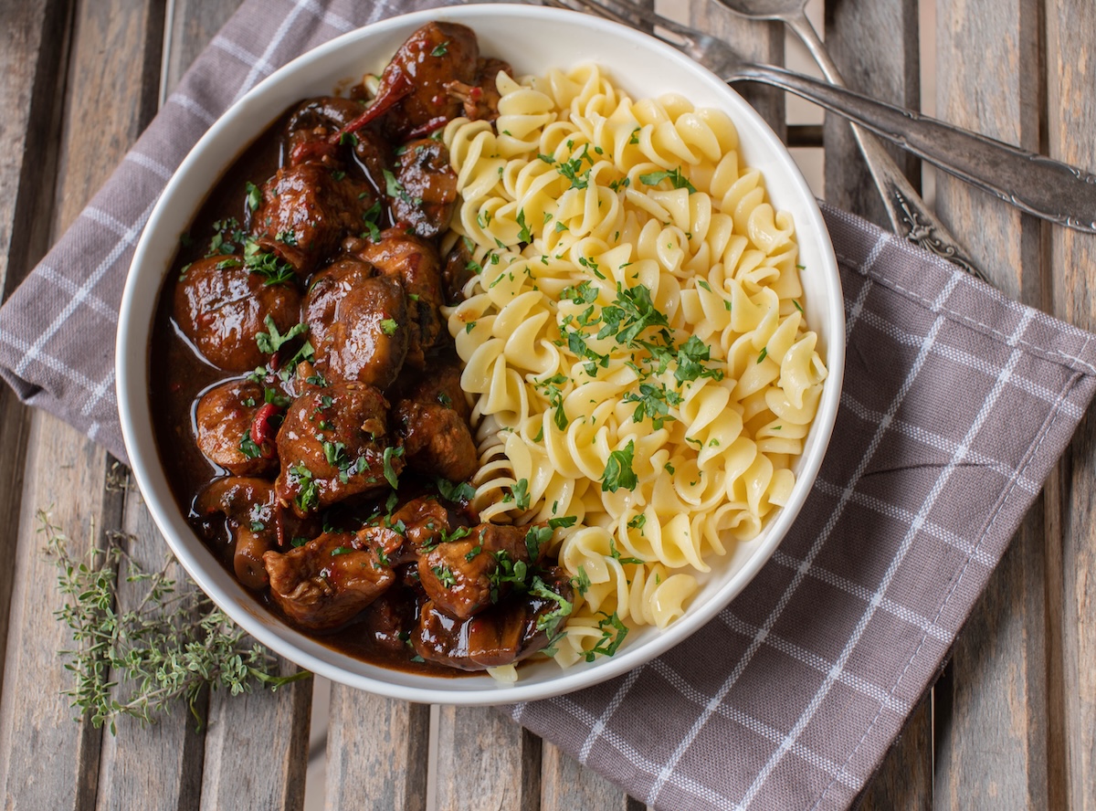 Ein Teller Brauhausgulasch mit Nudeln in der Draufsicht, der Teller steht auf einer karierten Serviette, daneben liegt Besteck.