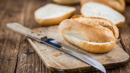 Ein aufgeschnittenes Brötchen, das im Airfryer aufgebacken wurde, auf einem Brett. Daneben ein Messer und im Hintergrund weitere Brötchen.