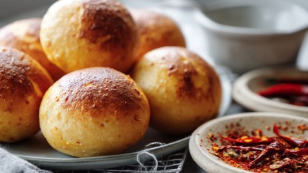Mehrere Chilibrötchen aufgestapelt auf einem Teller. Daneben Chilischoten in Schalen.