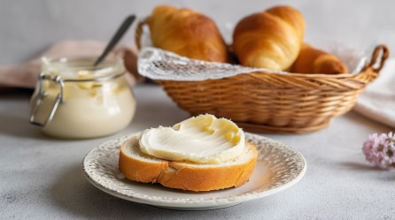 Eine Scheibe Baguette mit Eierlikör-Schoko-Aufstrich, dahinter ein Korb mit Croissants und ein Glas Aufstrich.