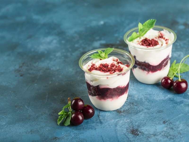 Zwei Dessertgläser Engelscreme mit Kirschen und Haselnuss-Crunch.