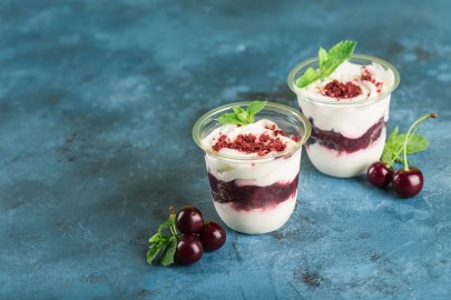 Zwei Dessertgläser Engelscreme mit Kirschen und Haselnuss-Crunch.