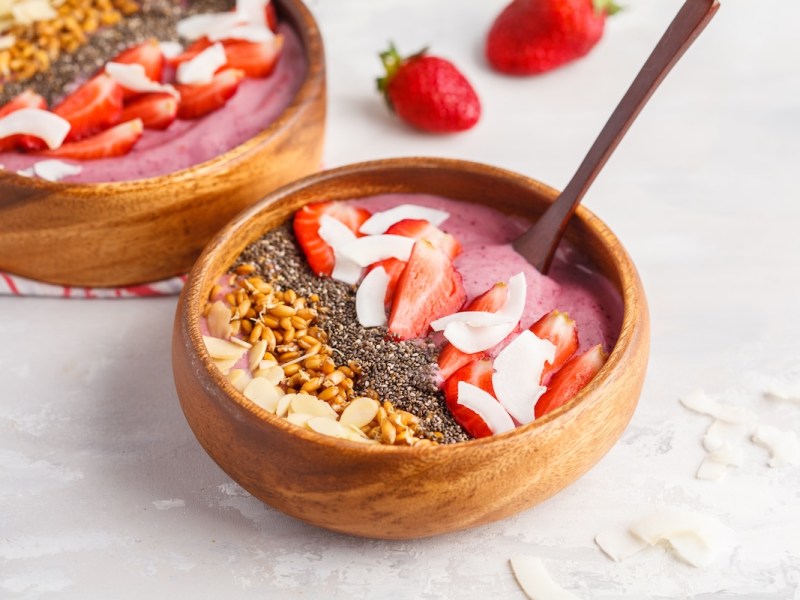 2 Erdbeer-Smoothie-Bowls mit Banan, garniert mit Erdbeeren, Nüssen und mehr.