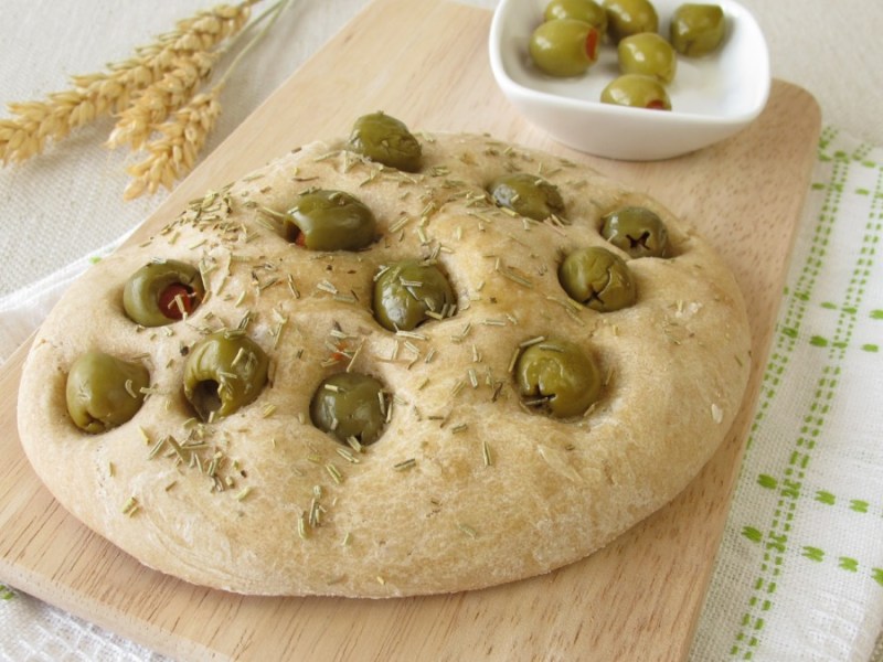 Eine Focaccia mit Oliven auf einem Holzbrett.