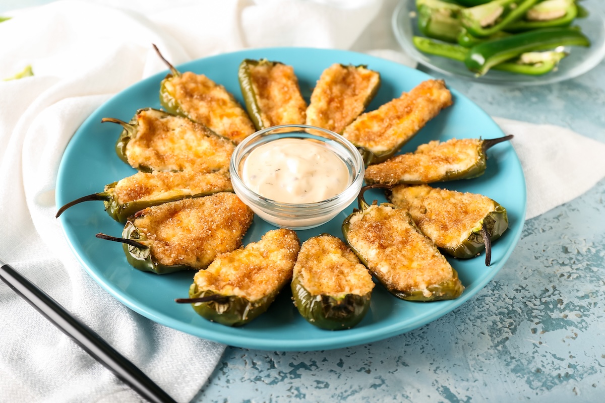 Ein Teller mit Jalapeño Poppers, überbackene grüne Chilischoten, in der Mitte steht eine Dip-Schale.