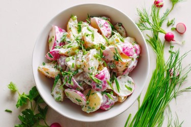 Schale mit Kartoffel-Radieschen-Salat und Kräuter daneben