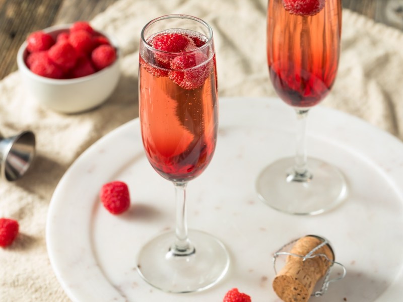 Zwei Gläser Kir Royal mit Himbeeren auf einem weißen Marmortablett.