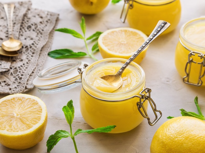 Lemon Curd selbst machen: Ein Glas Lemon Curd zwischen allerlei Zutaten.
