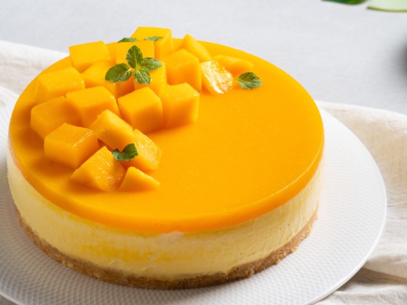 Ein Mango-Käsekuchen auf einer runden Kuchenplatte.