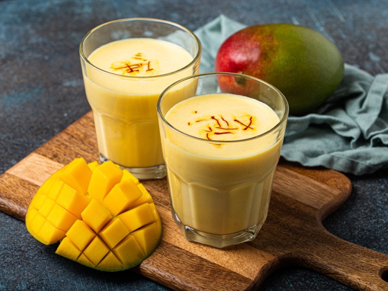 Zwei Gläser mit Mango Lassi, garniert mit Safranfäden, auf einem Holzbrett.