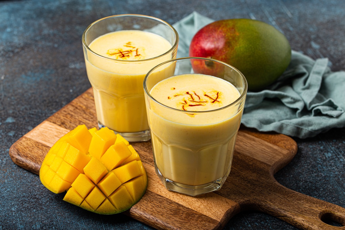 Zwei Gläser mit Mango Lassi, garniert mit Safranfäden, auf einem Holzbrett.