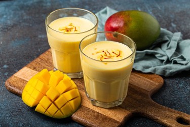 Zwei Gläser mit Mango Lassi, garniert mit Safranfäden, auf einem Holzbrett.