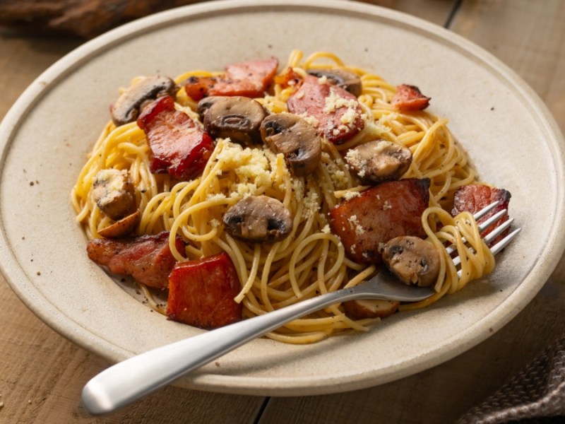Ein Teller Pasta mit Speck und Pilzen.