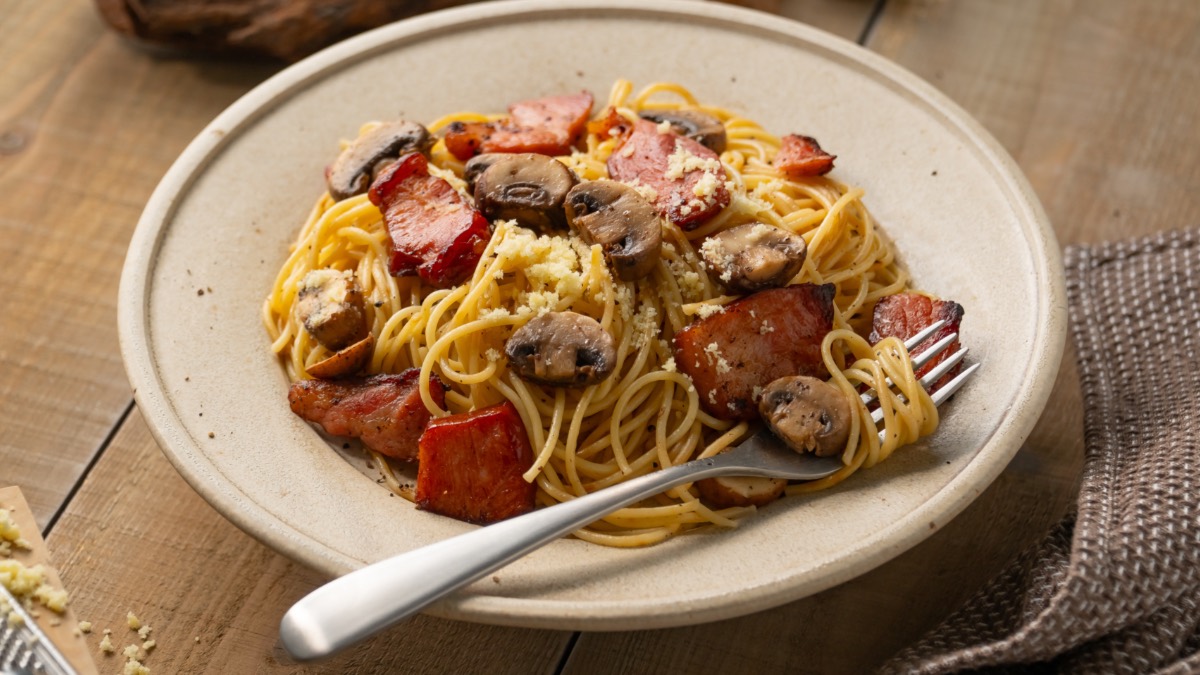 Ein Teller Pasta mit Speck und Pilzen.