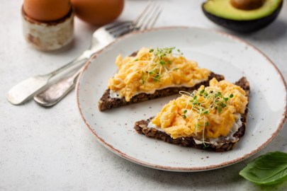 Zwei Brotscheiben mit Rührei mit Quark auf einem hellen Teller. Das Ei ist mit Sprossen garniert.