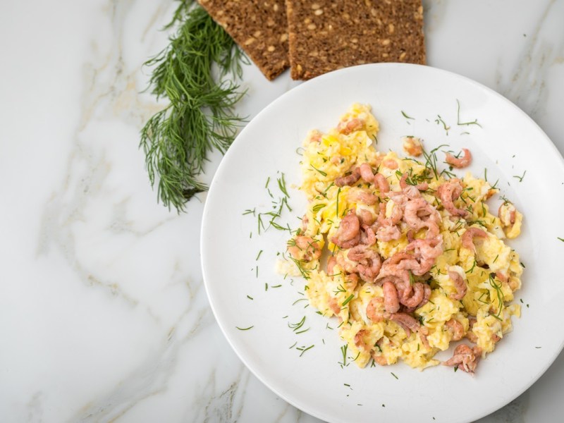 Teller mit Rührei mit Krabben und Schwarzbrot daneben