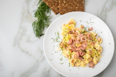 Teller mit Rührei mit Krabben und Schwarzbrot daneben