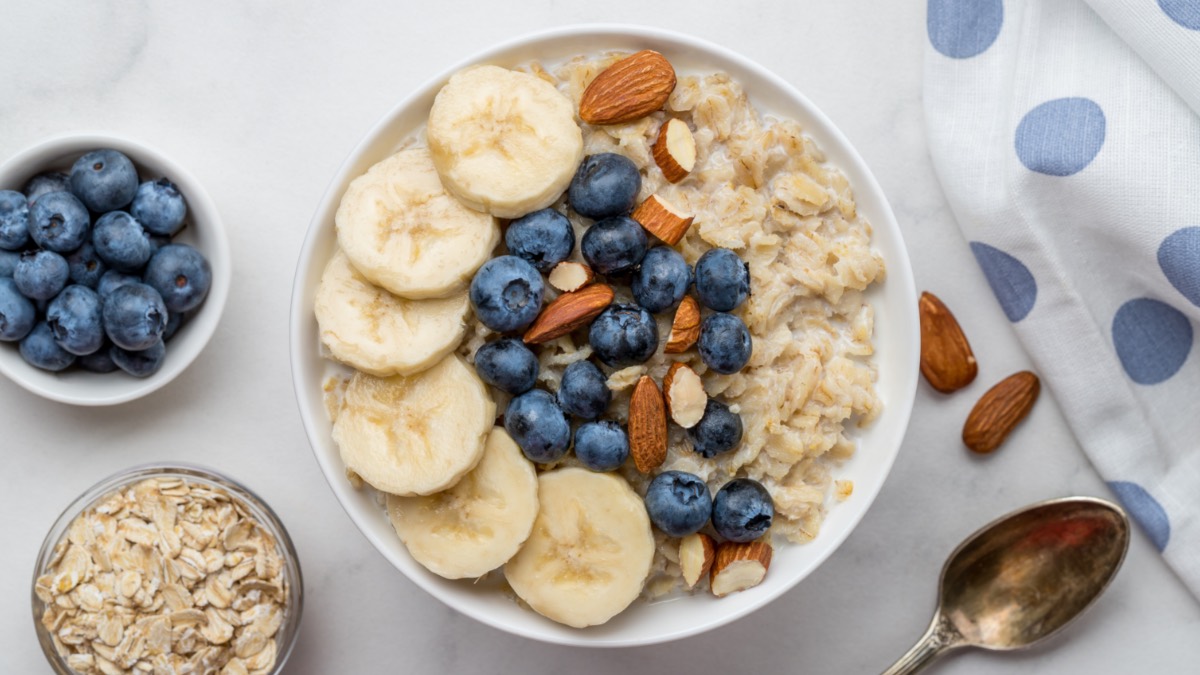 Eine Schüssel Soja-Porridge mit Bananen, Blaubeeren und Mandeln in der Draufsicht.