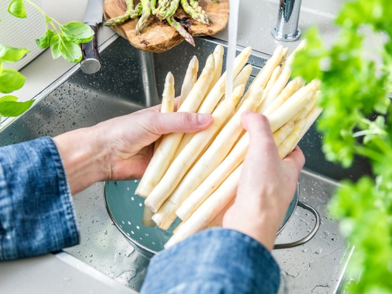 Spargel kochen: ein Mann wäscht weißen Spargel über der Spüle.
