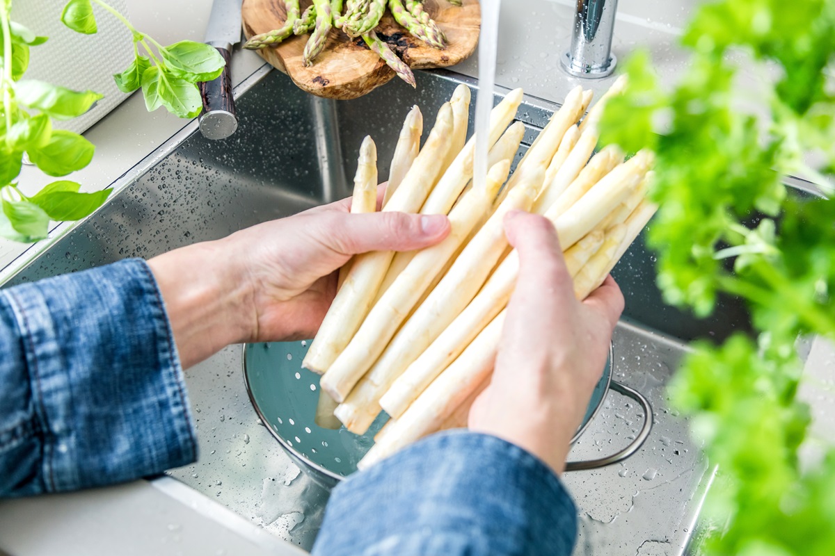 Spargel kochen: ein Mann wäscht weißen Spargel über der Spüle.