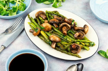 Spargel-Pilz-Pfanne auf einem ovalen Teller, daneben Besteck und eine Schale Feldsalat.