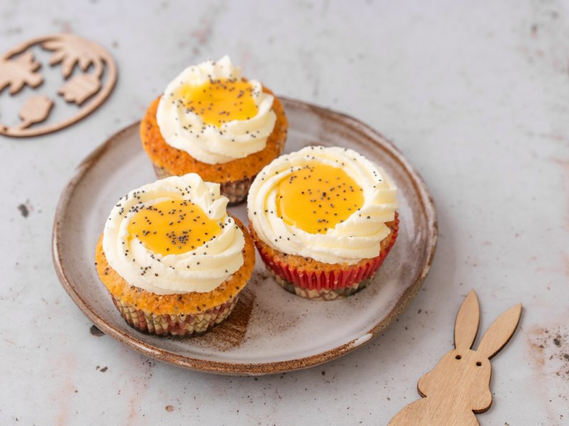 Drei Spiegelei-Cupcakes auf einem Teller. Daneben liegt ein Holz-Osterhase.