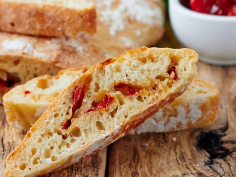 Mehrere Scheiben Tomaten-Ciabatta, die vor dem Brot liegen.