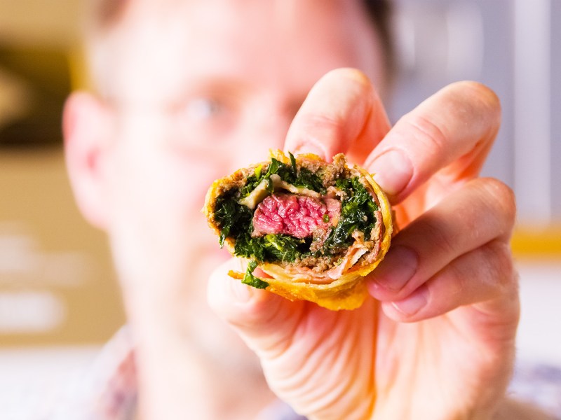 Eine Beef Wellington Frühlingsrolle wird in die Kamera gehalten und gibt den Blick auf die Füllung frei.