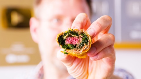 Eine Beef Wellington Frühlingsrolle wird in die Kamera gehalten und gibt den Blick auf die Füllung frei.